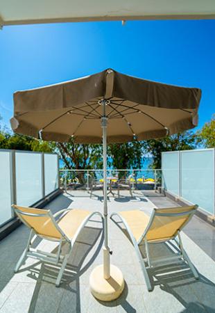 Terrazza con sdraio e ombrellone, vista mare e cielo azzurro.