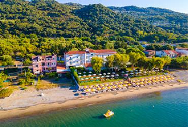 Spiaggia con ombrelloni, hotel sullo sfondo, circondato da colline verdi e mare calmo.